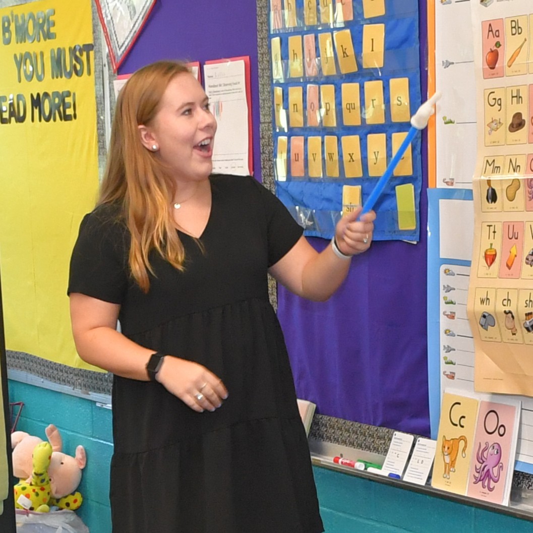 Teacher pointing to chalkboard while students raise their hands